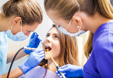 A dental hygienist performing oral care on a patient while other dental professionals observe.